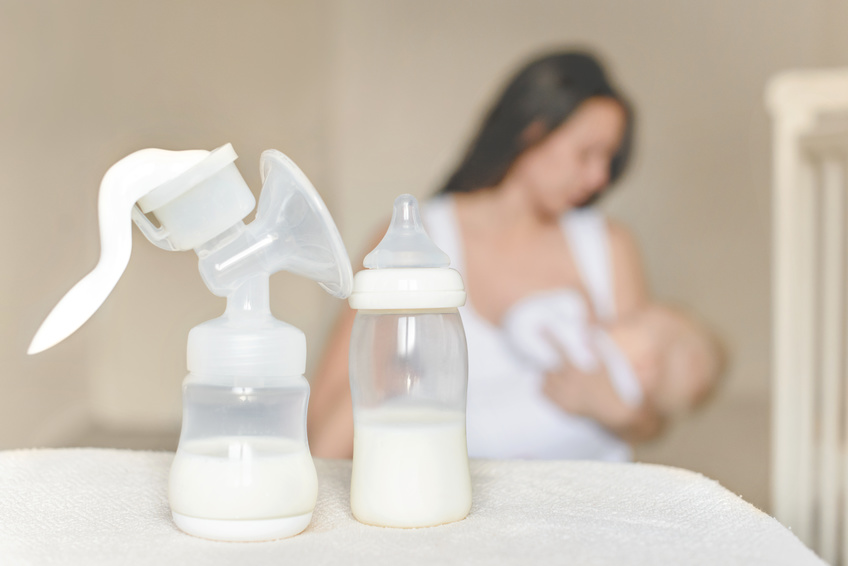 Manual breast pump and bottle with breast milk on the background of mother holding in her hands and breastfeeding baby.